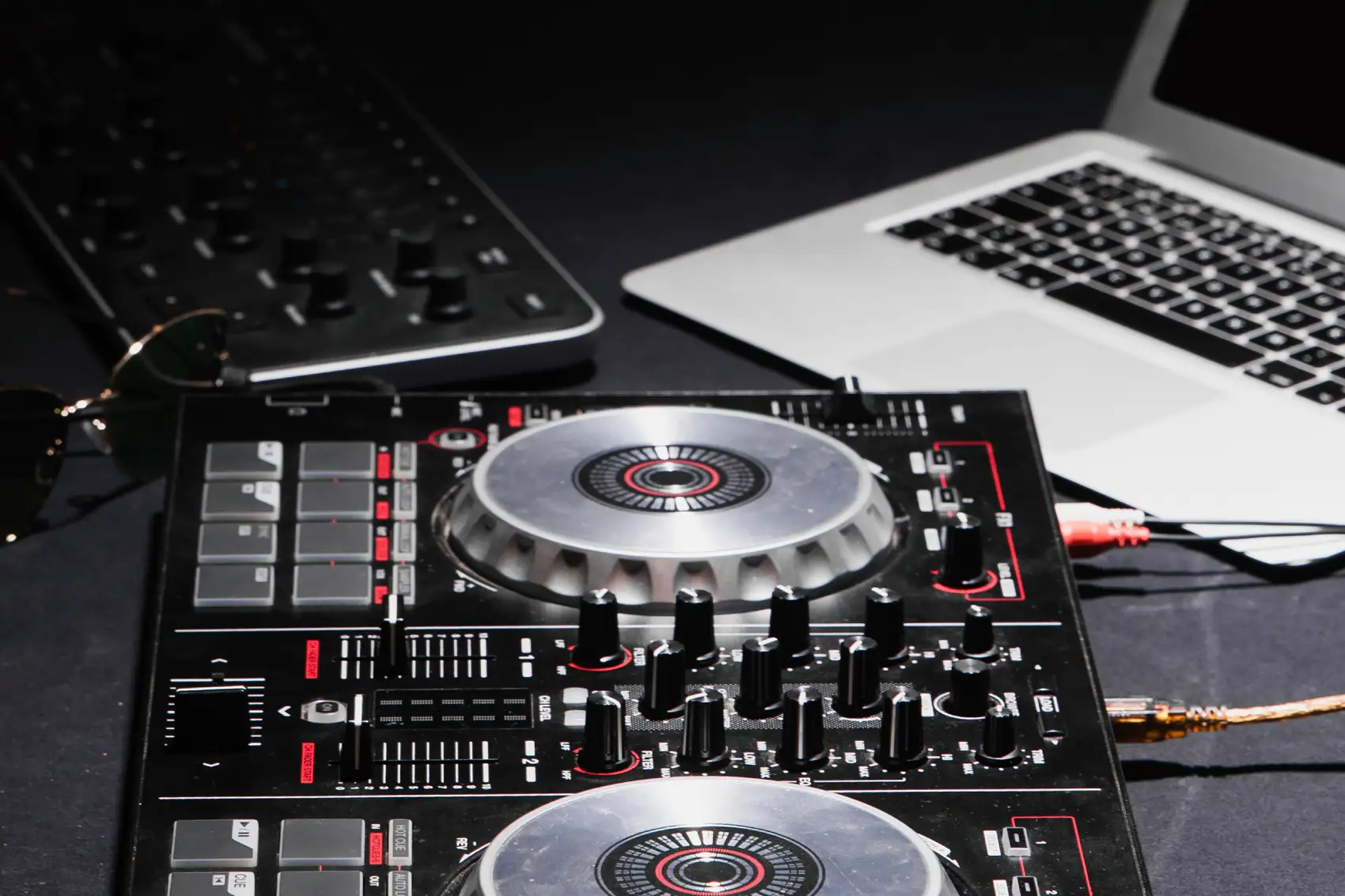 Kontroler DJ-ski z pokrętłami i tShield na biurku obok laptopa oraz okularów